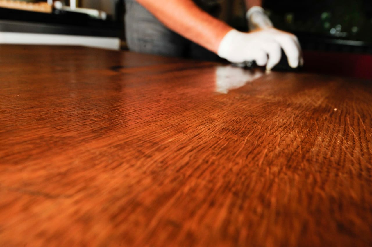 Gloved hand working a fresh coat across a countertop until the surface reads as an even, deep gloss