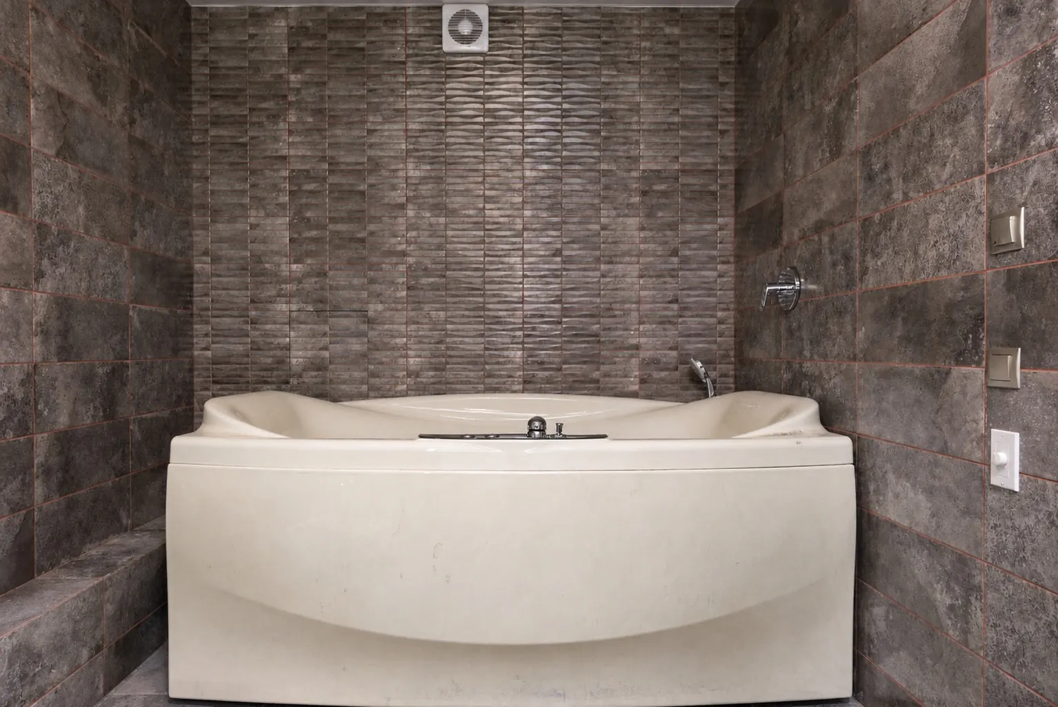 Stone-tiled soaking tub with a dull, yellowed shell and light wear before refinishing